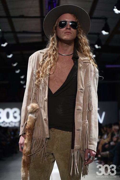 A man wearing a hat and sunglasses is walking down a runway.