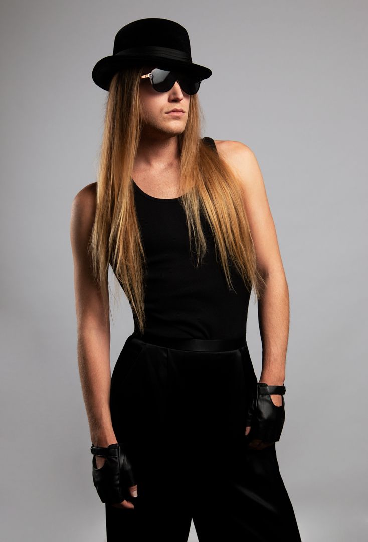 A woman with long hair is wearing a hat and sunglasses for a photoshoot.