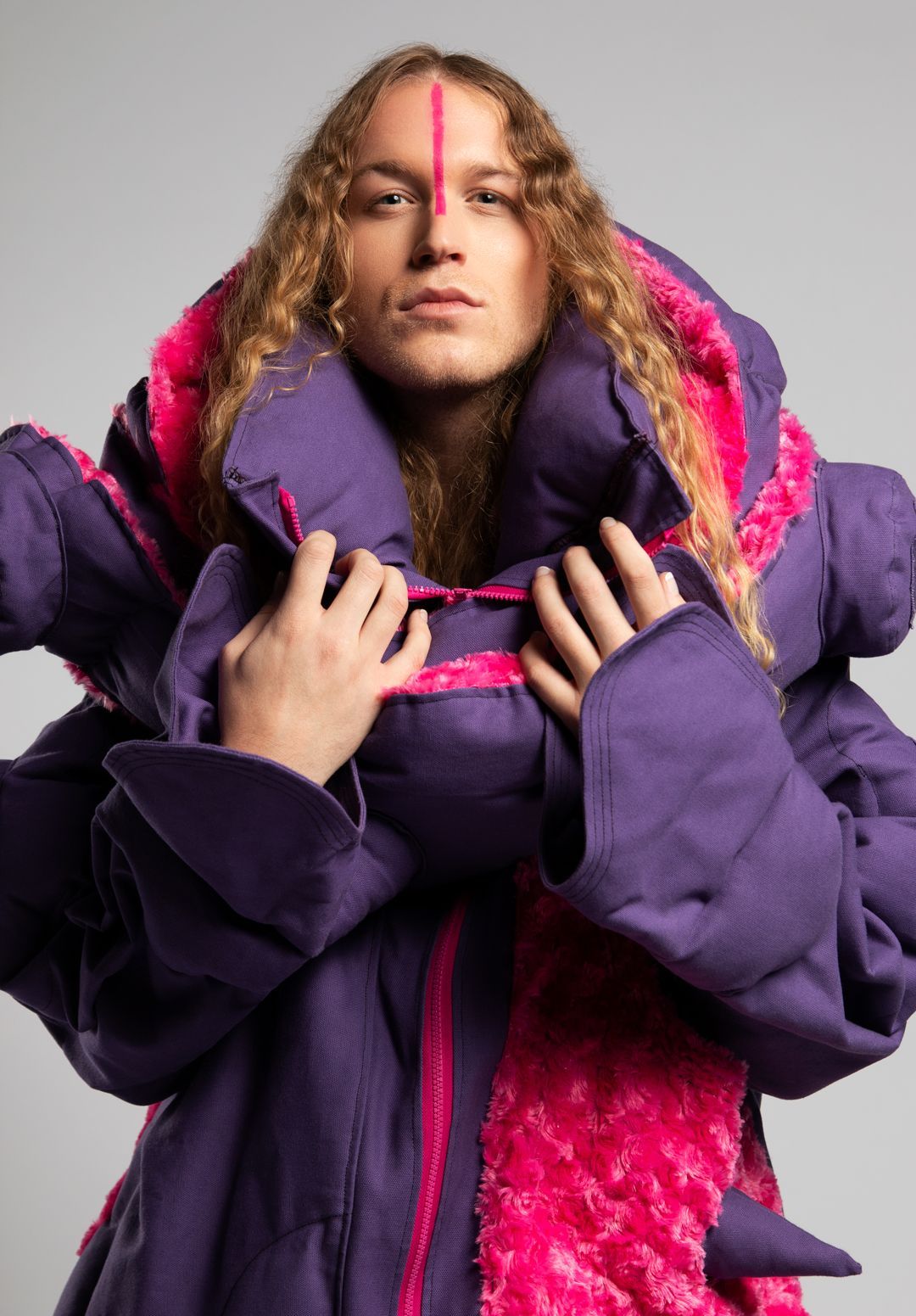 A woman with curly hair is wearing a purple and pink coat.