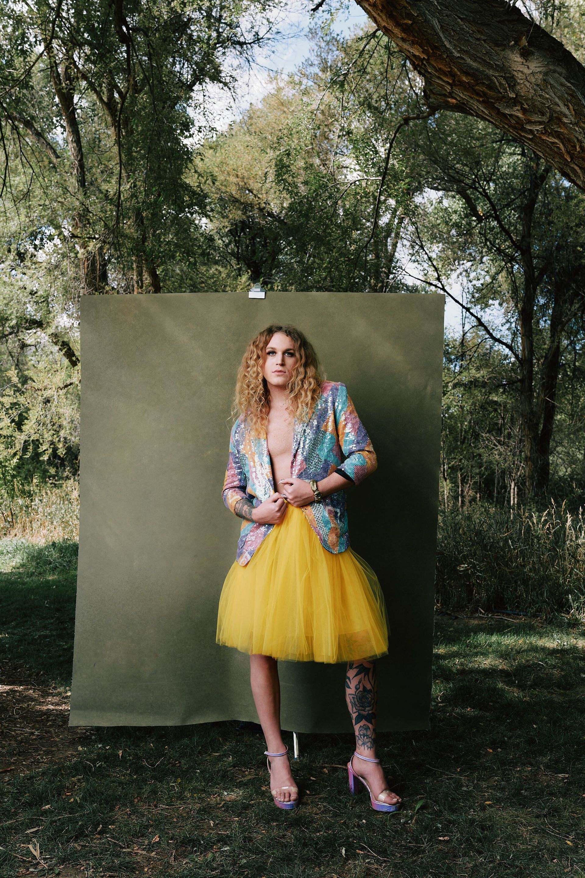Scotty in a yellow tulle skirt is standing in front of a green wall for a fashion photo shoot.