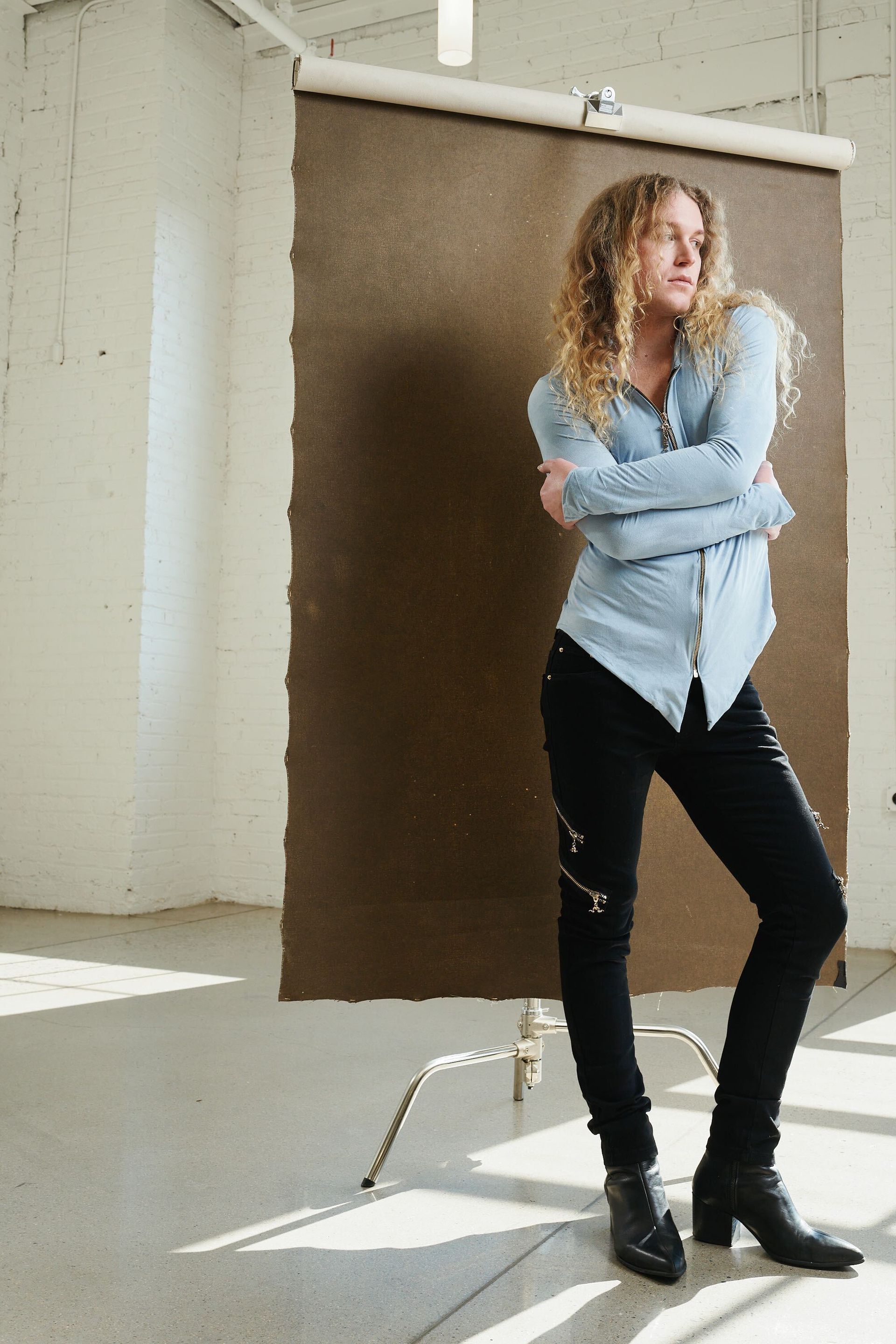 Scotty is standing in front of a brown wall with her arms crossed for a fashion photo shoot.