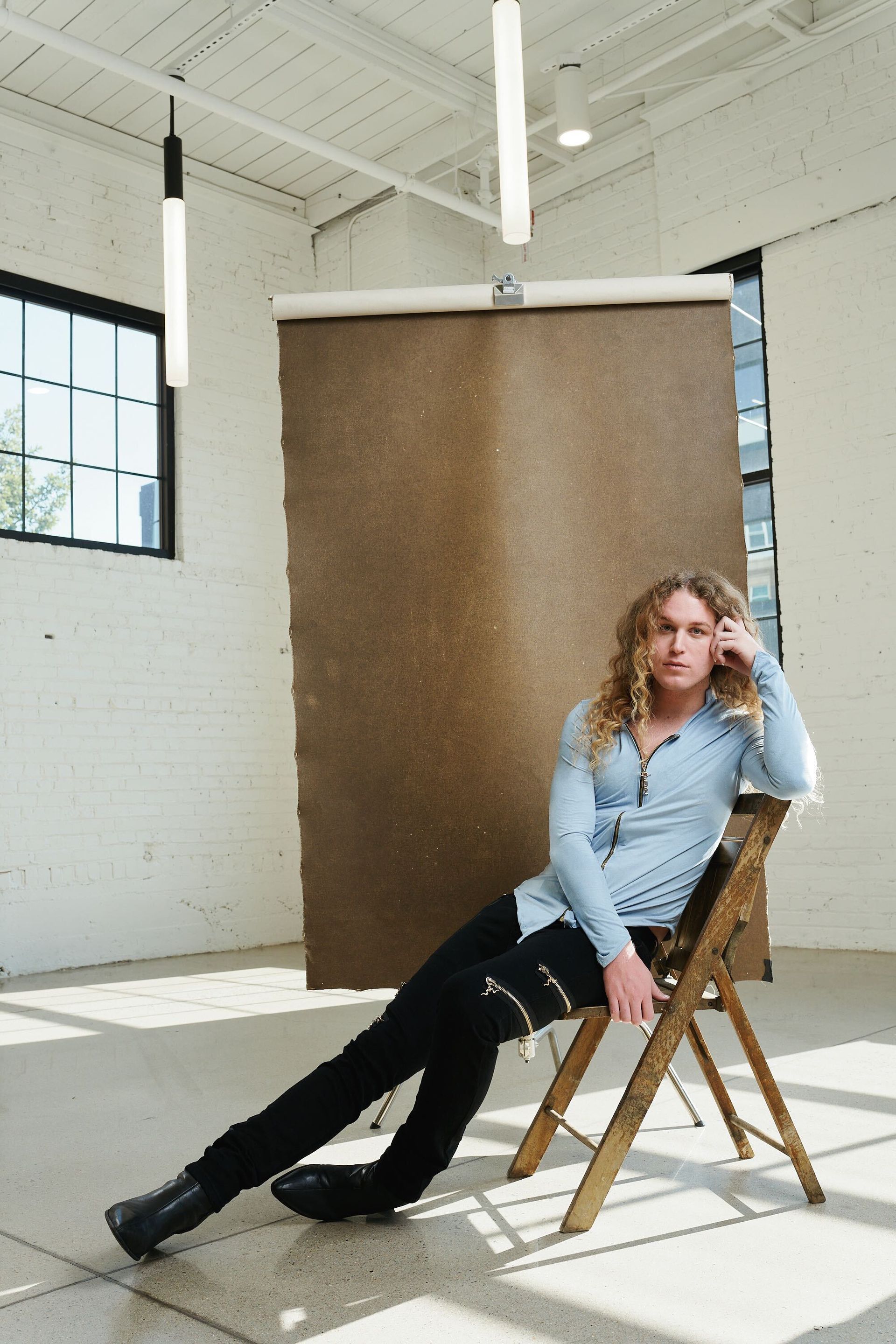 Scotty is sitting on a wooden chair in a room for a fashion photo shoot.