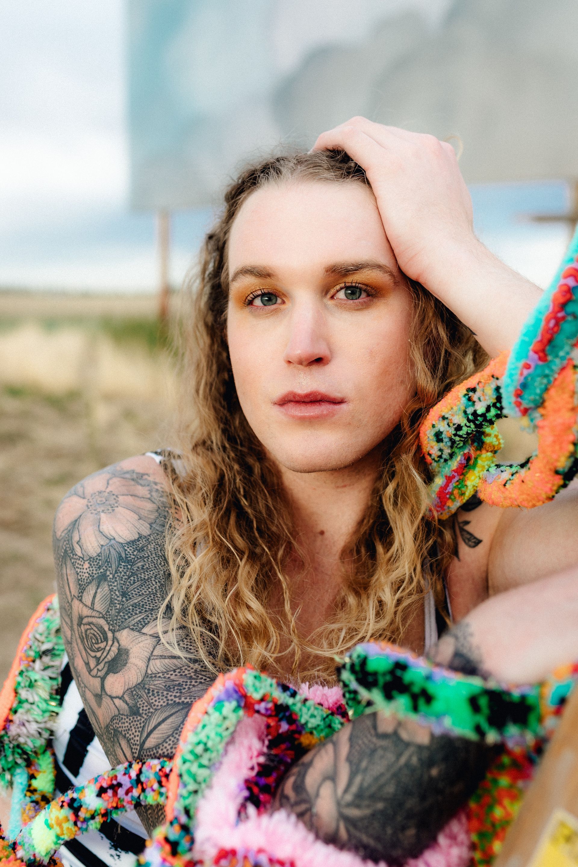 Scotty with a tattoo on their arm is sitting on the ground holding her hand to her head.