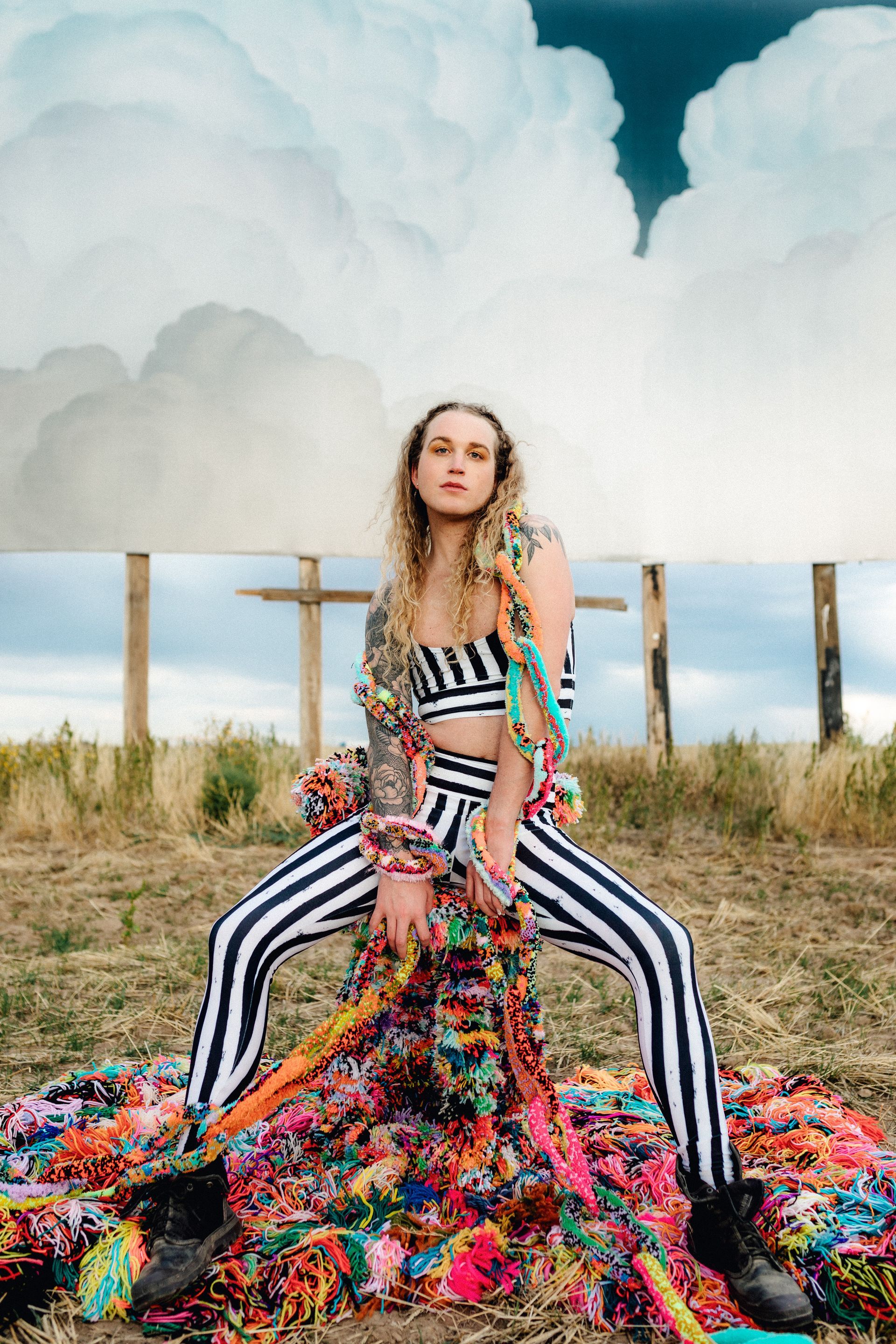 Scotty is sitting on a pile of colorful yarn in a field for a fashion photo shoot.