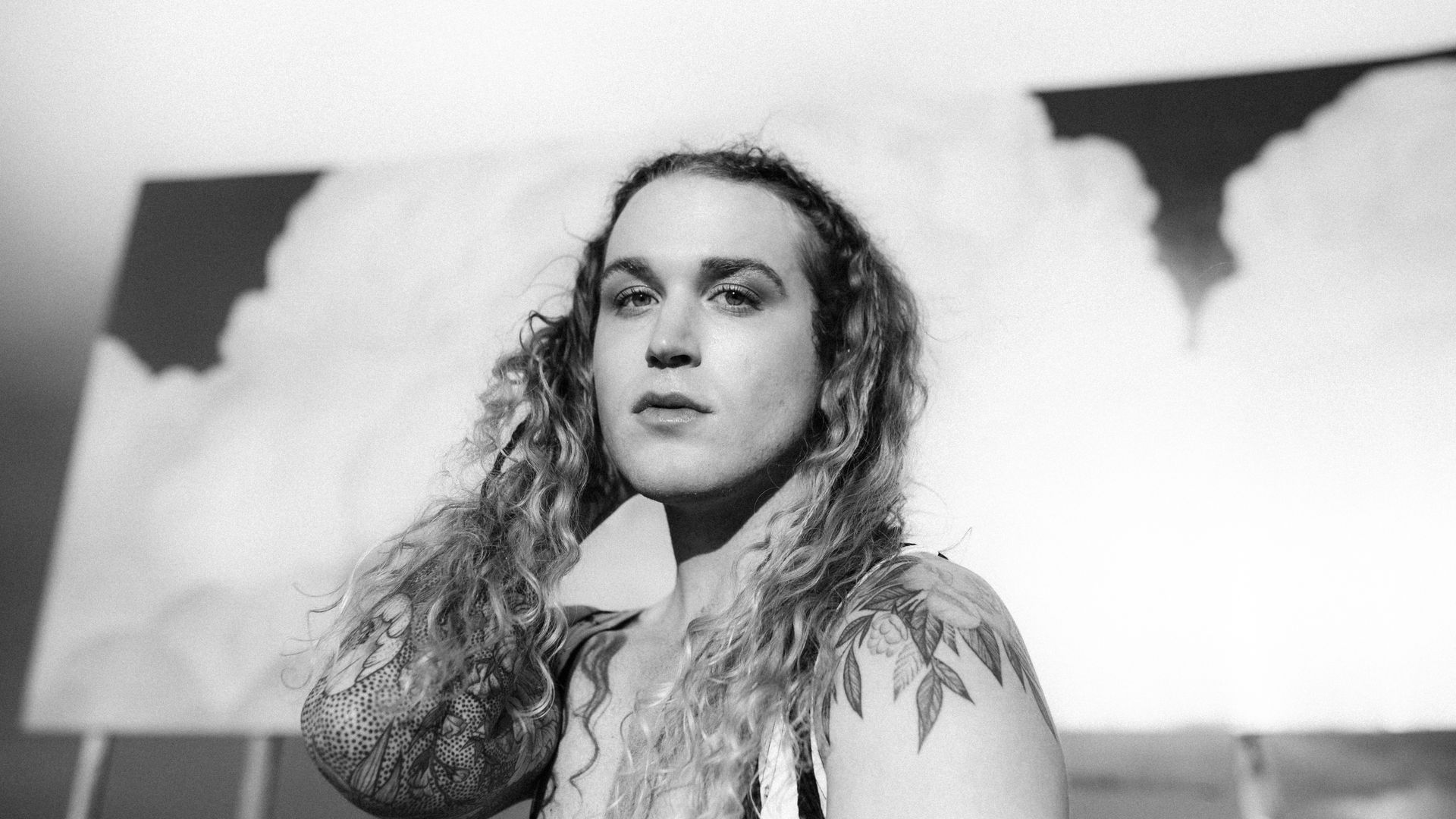 A black and white photo of Scotty with long hair and a tattoo on their arm.