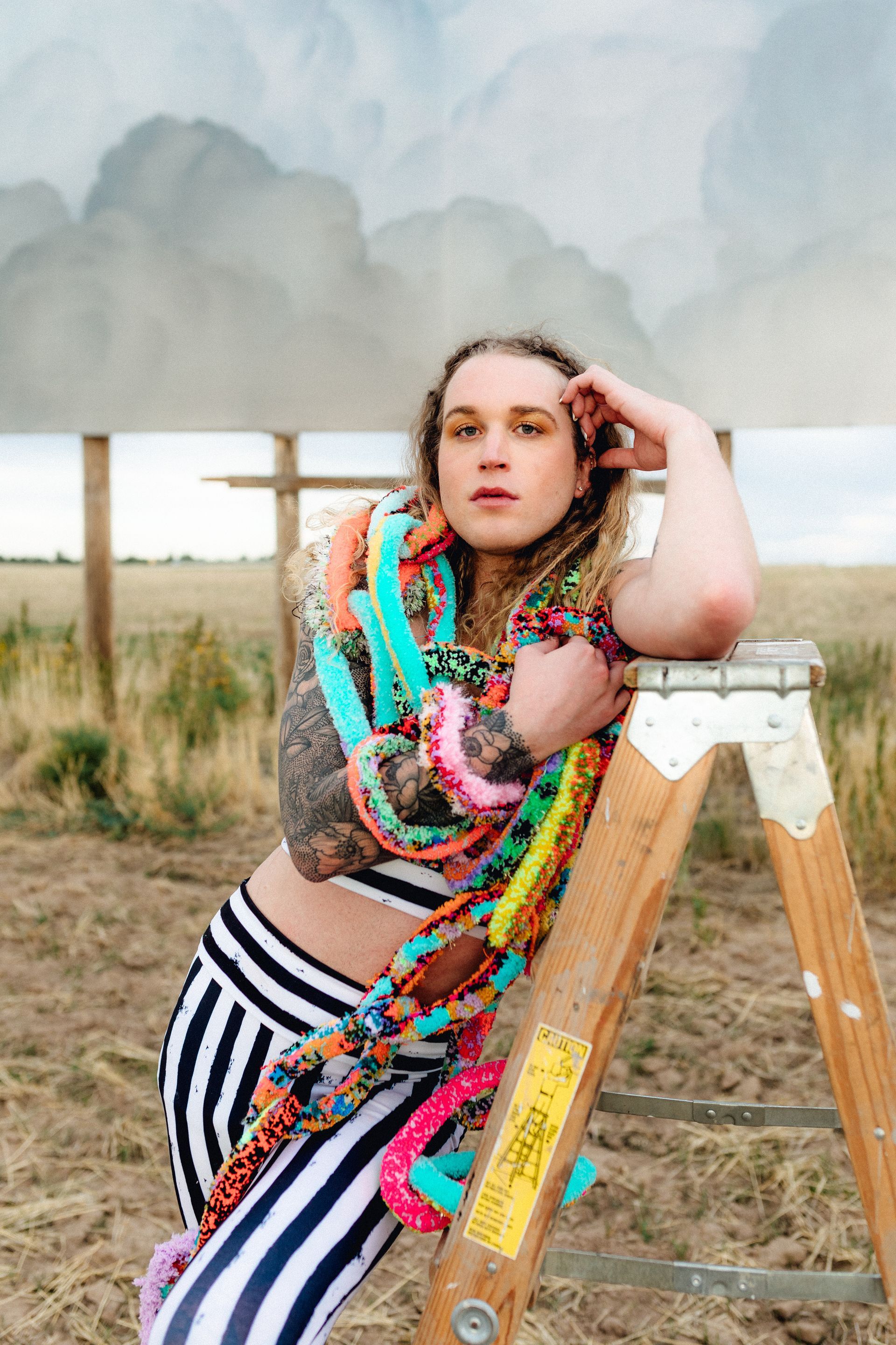 Scotty leaning on a wooden ladder in a field for a fashion photo shoot.