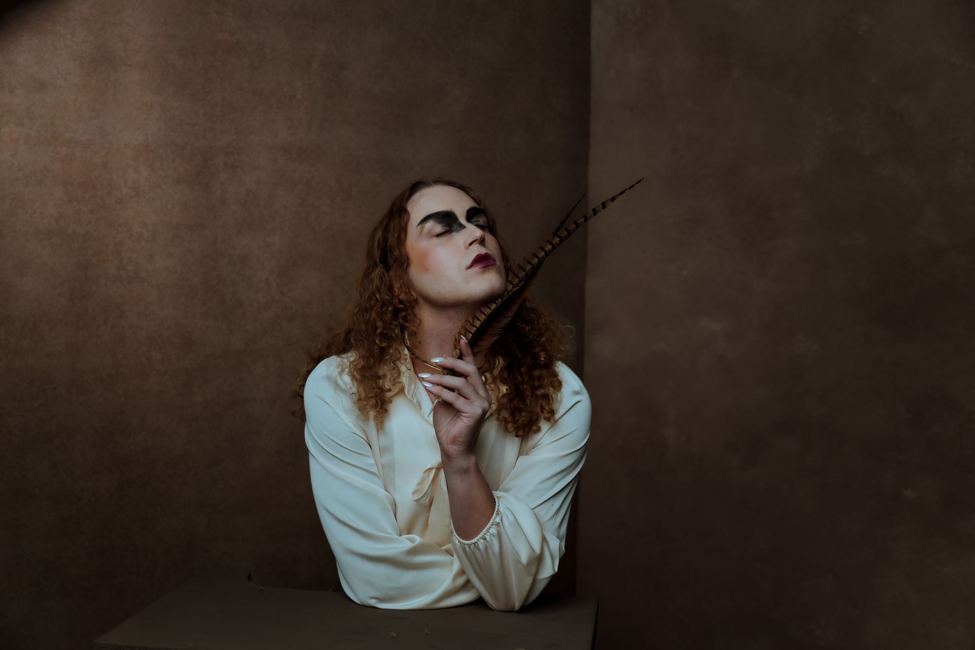 A woman in a white shirt is holding a feather in her hand for a fashion photo shoot.