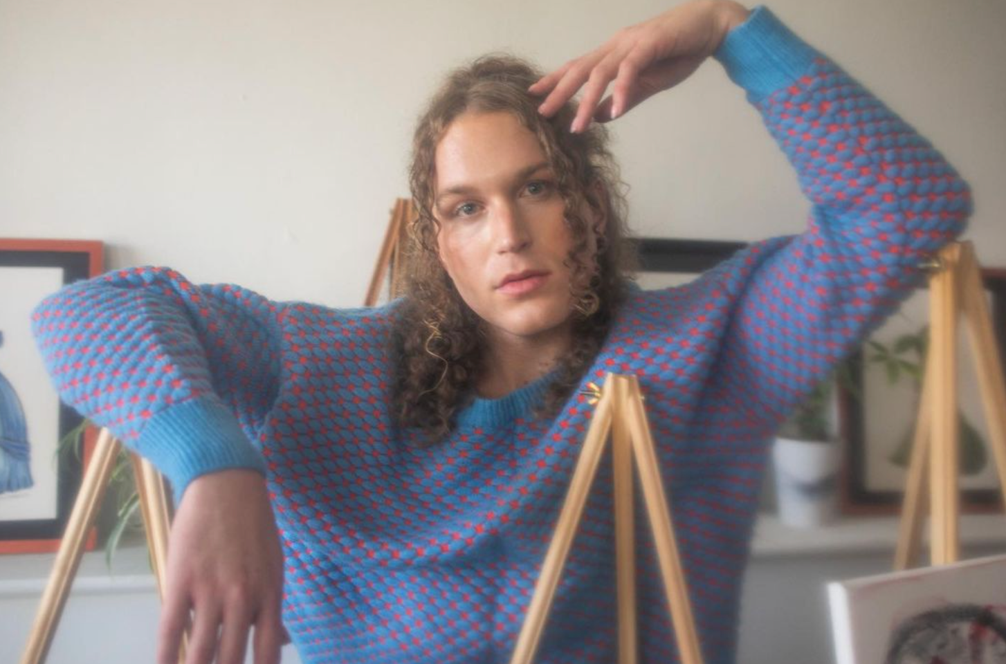 A man in a blue and red sweater is standing next to a wooden easel for a fashion photo shoot.