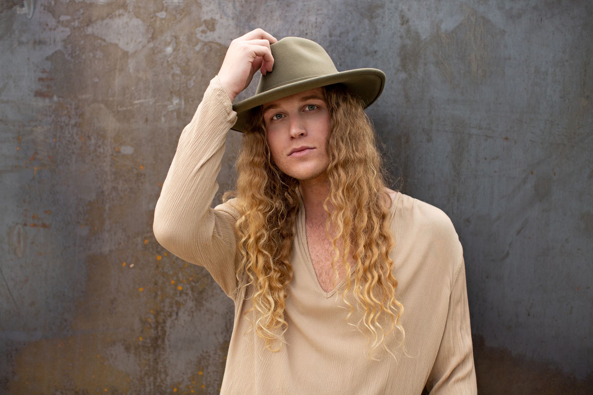 A young man with long hair is wearing a hat and a sweater for a fashion photo shoot.