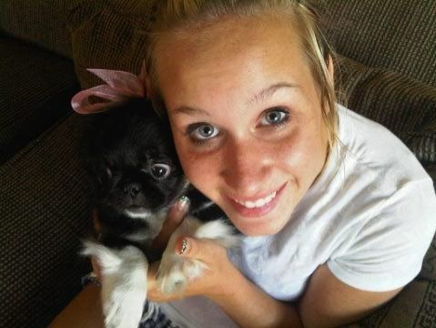 Woman smiling, holding small black and white dog with pink bow.