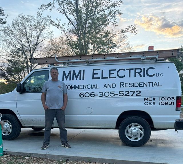Man standing beside a white MMI Electric service van with ladder rack at dusk.