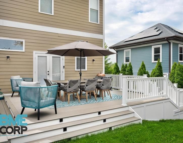 Back deck with outdoor dining set, umbrella, white railing, and blue-gray chairs beside a tan house.