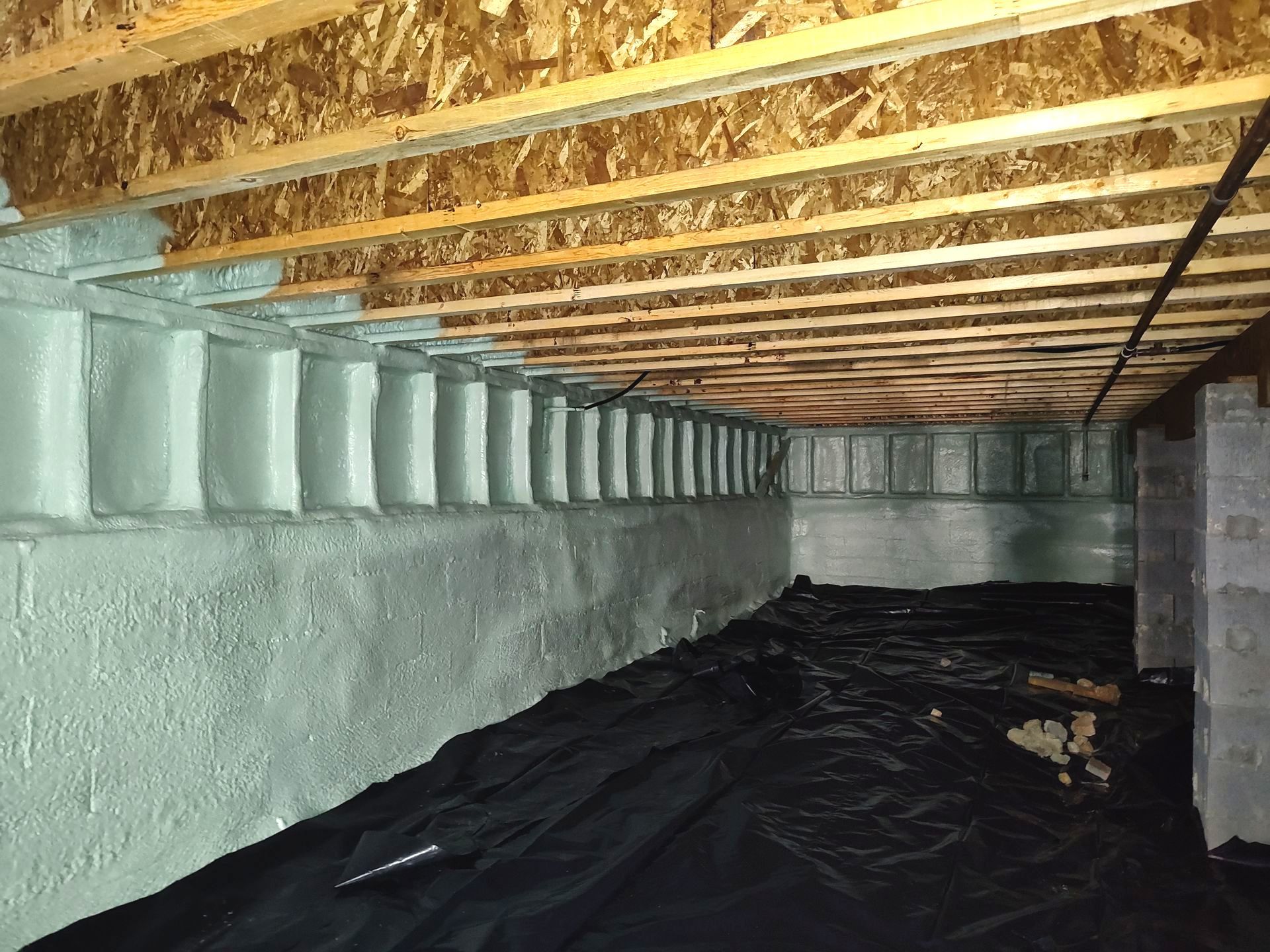 A basement with a wooden ceiling and a black tarp on the floor.