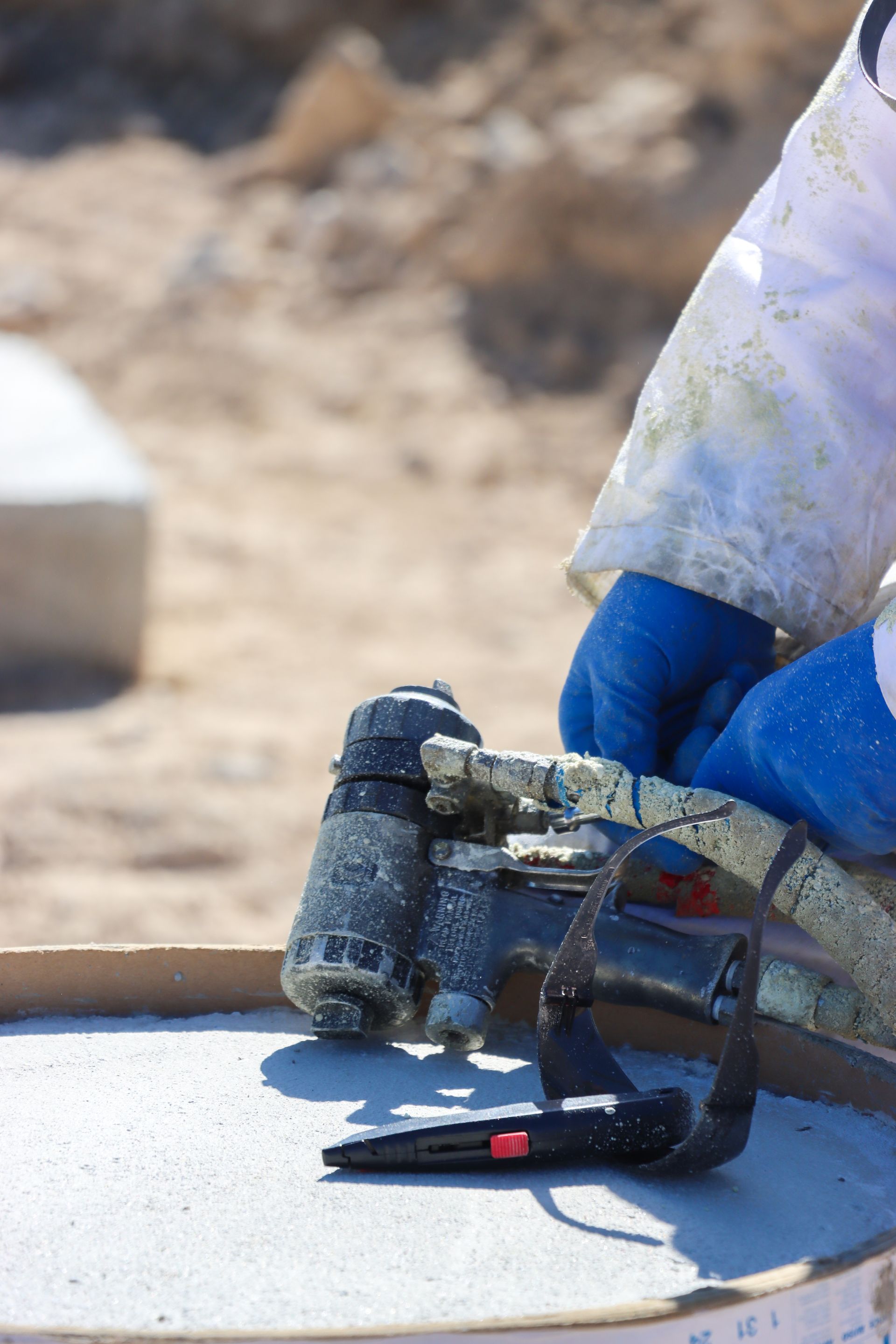 A person wearing blue gloves is holding a tool on a table.