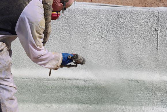 A man wearing a mask is spraying concrete on a wall.