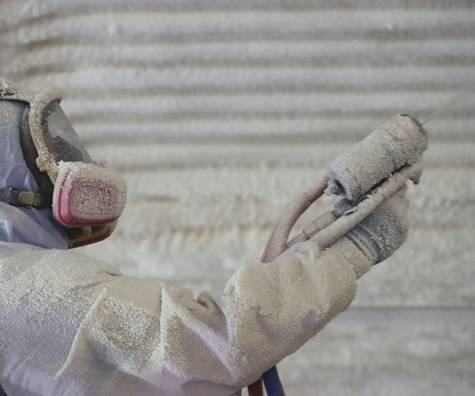 A man wearing a gas mask is painting a wall.