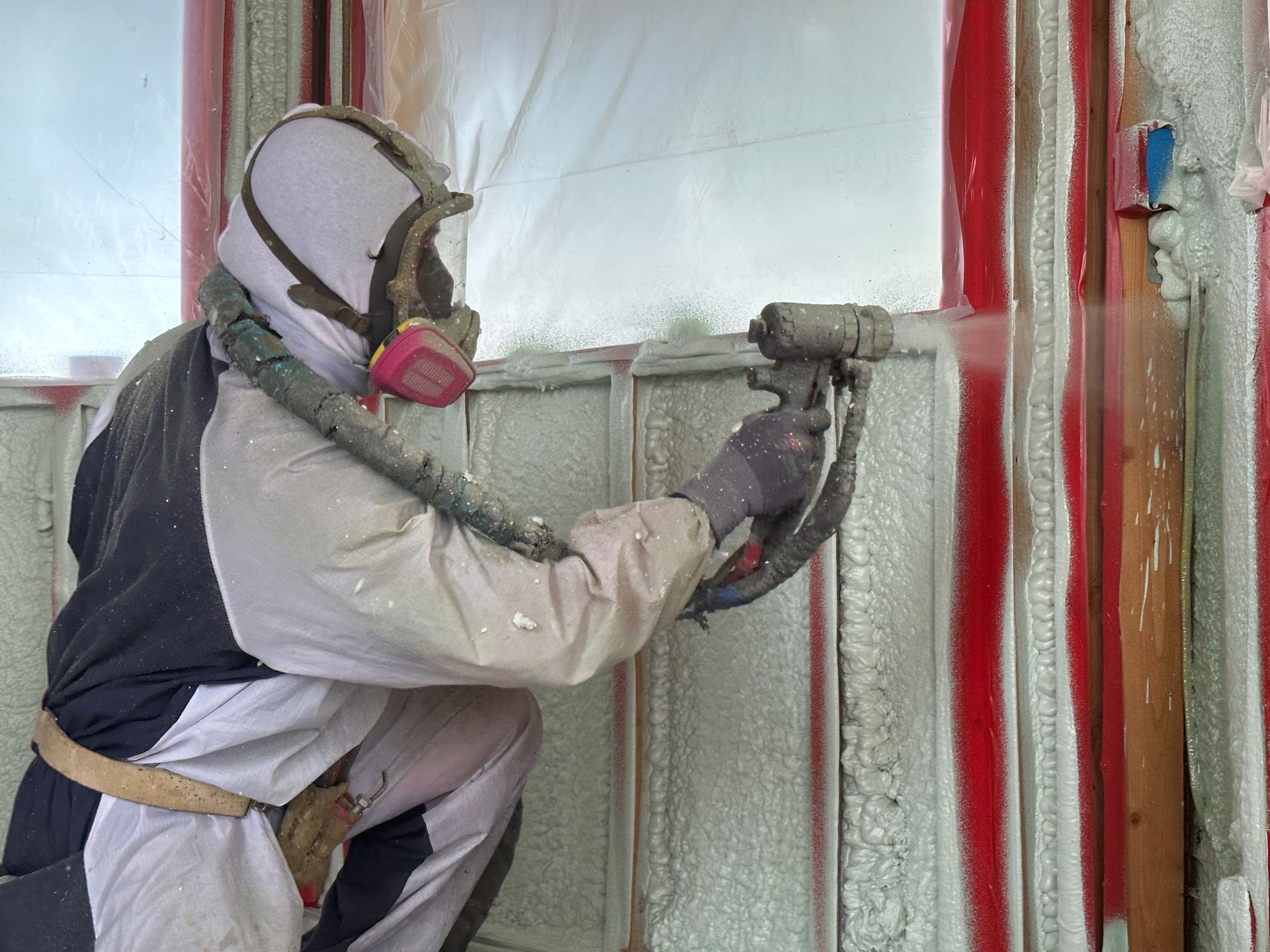 A man wearing a gas mask is spraying foam on a wall.