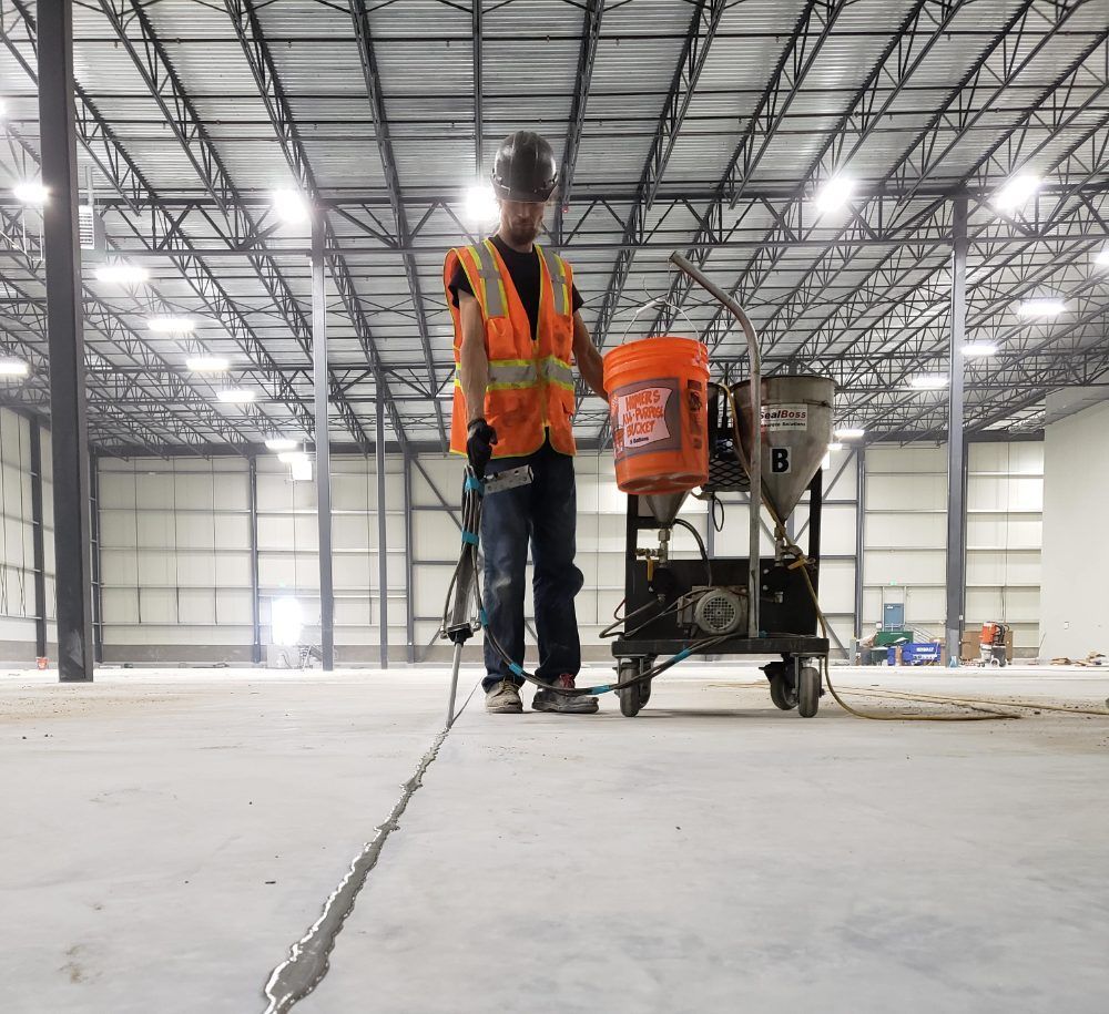 A man is working on a concrete floor in a large warehouse.