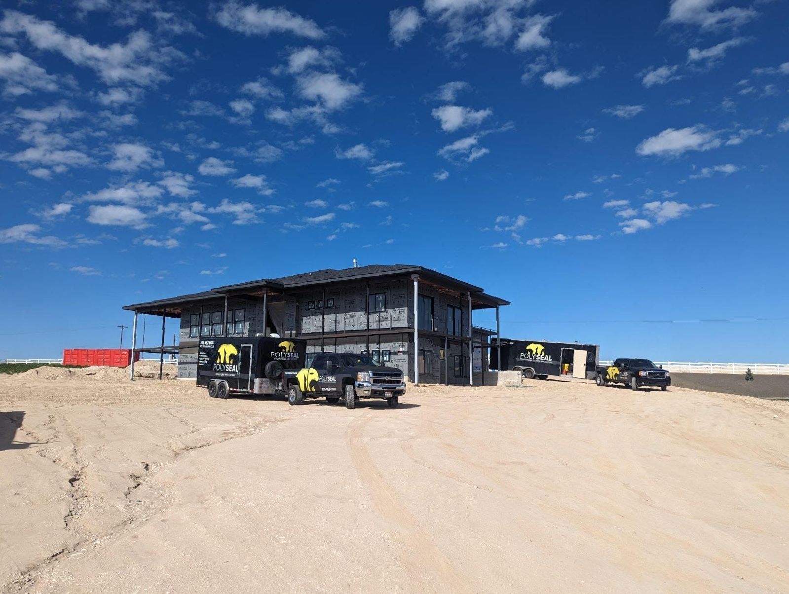 A large house is being built in the desert with trucks parked in front of it.