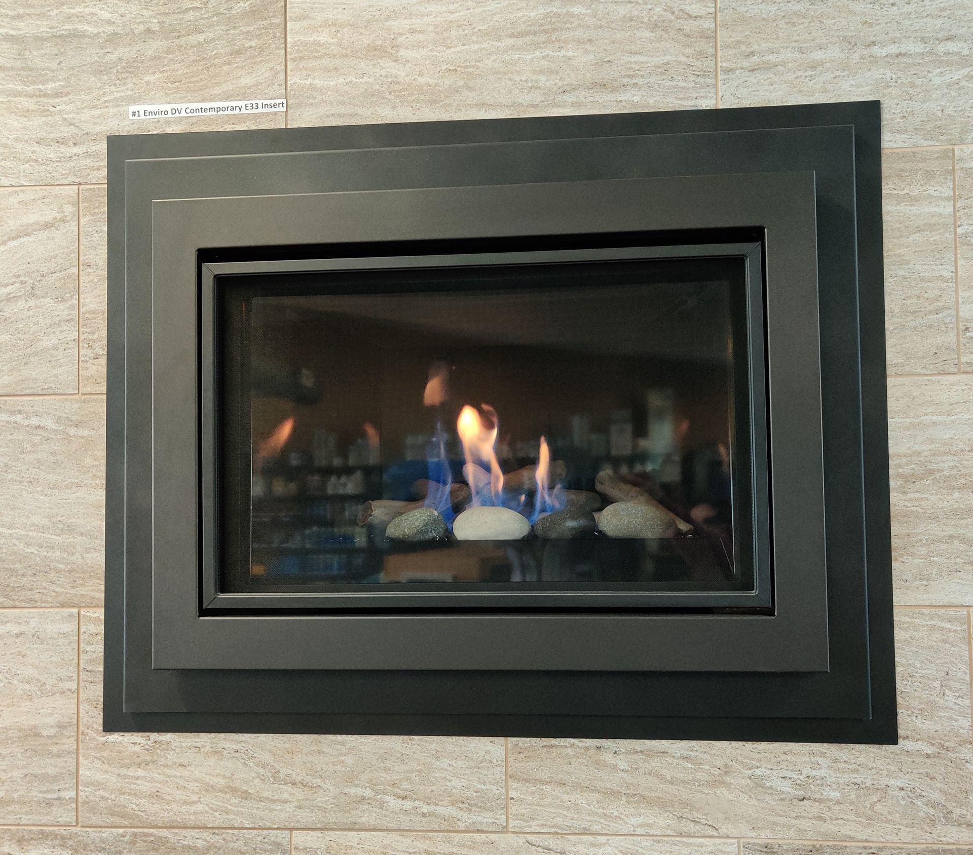 Gas fireplace burning inside a black metal frame, set in a tiled wall.