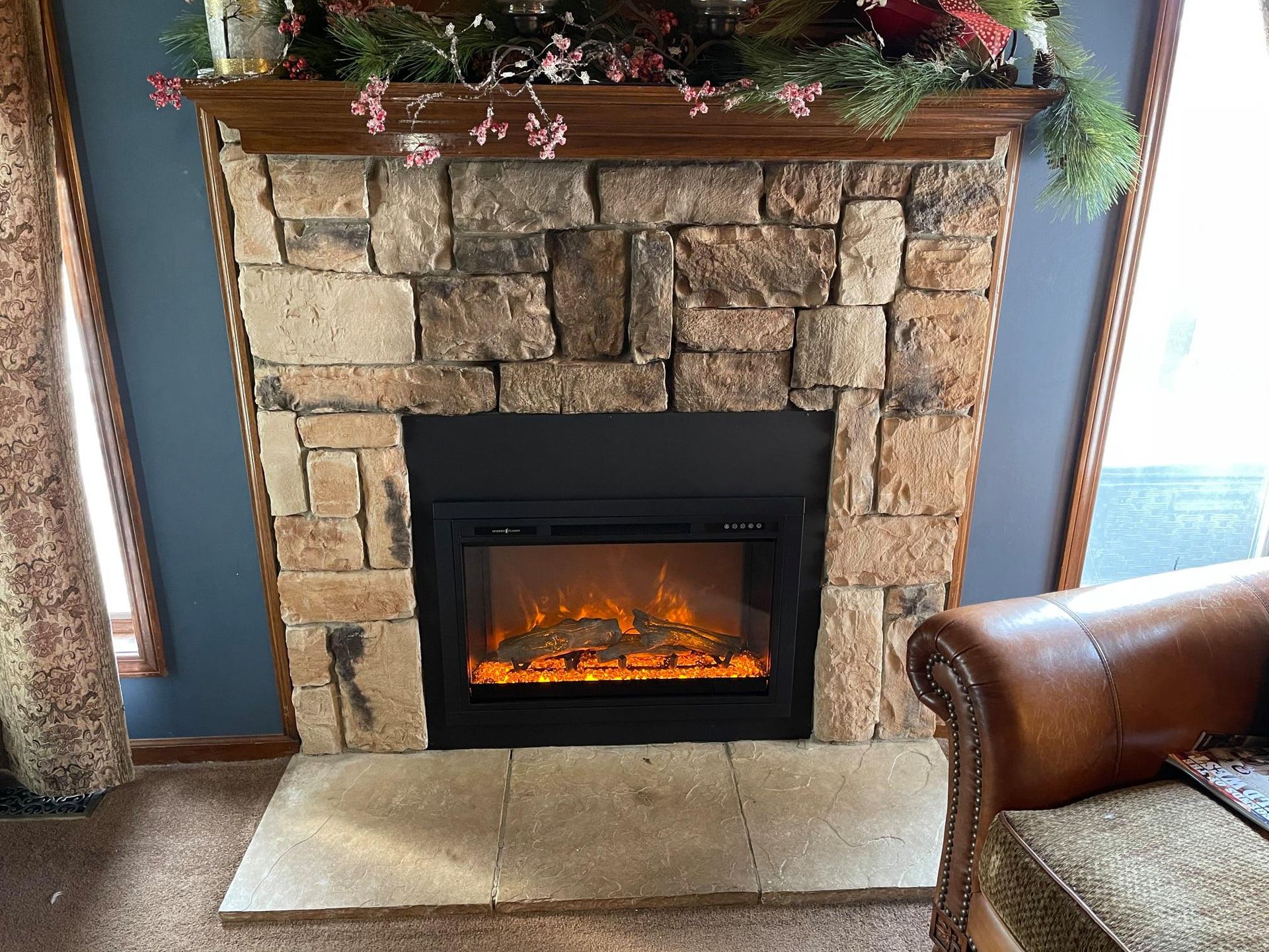 Fireplace with a stone facade, a lit electric fire, and wooden mantel with floral decorations.