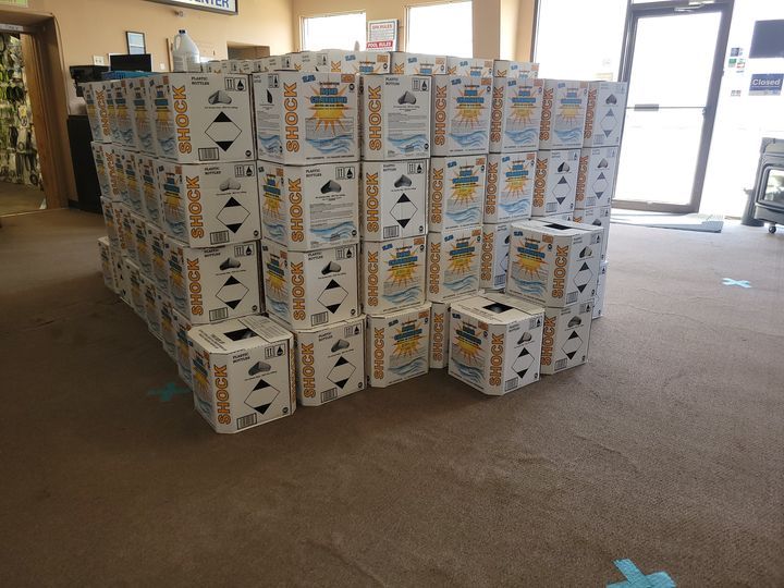 Stack of pool shock boxes inside a store, stacked on carpet.