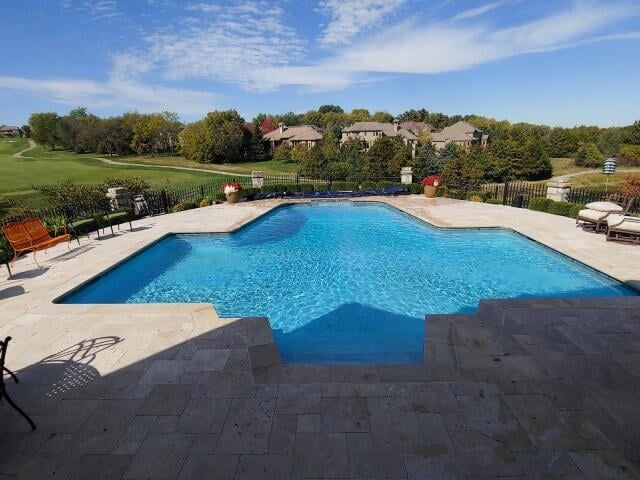 Swimming pool with blue water, beige stone patio, and golf course in the background under a blue sky.