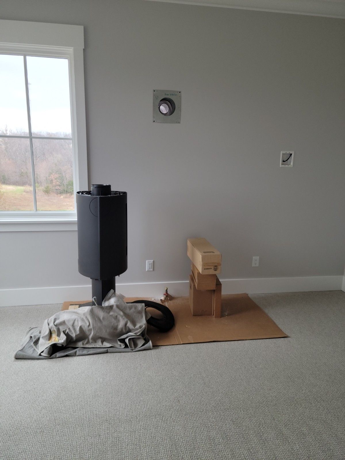 Black stove and materials on cardboard in a room with a window and gray walls.