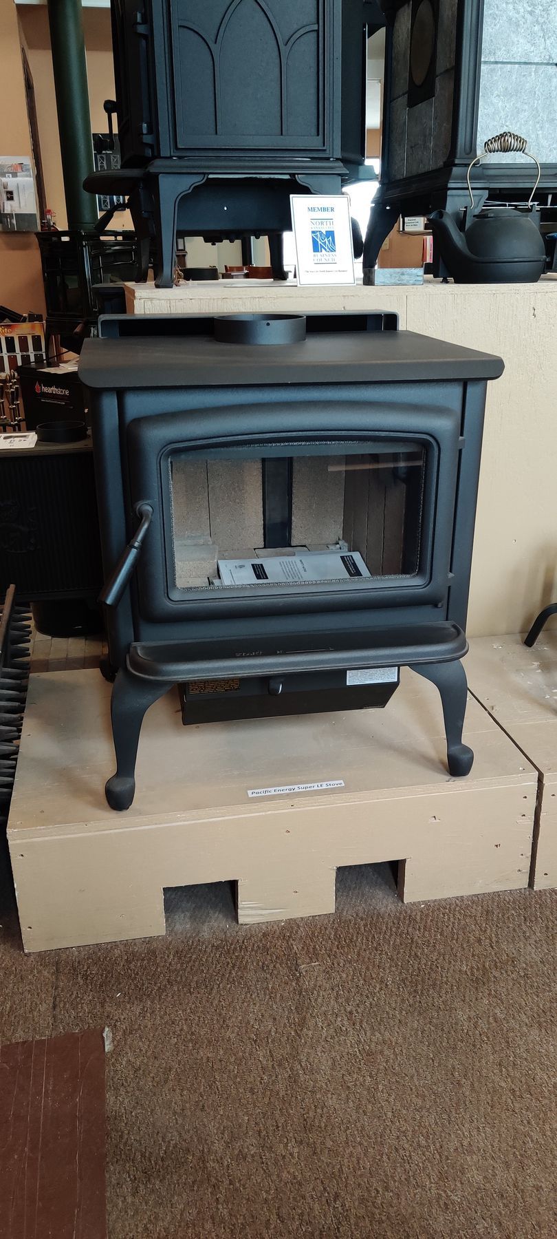 Black wood-burning stove with open door on a cardboard base, in a showroom setting.