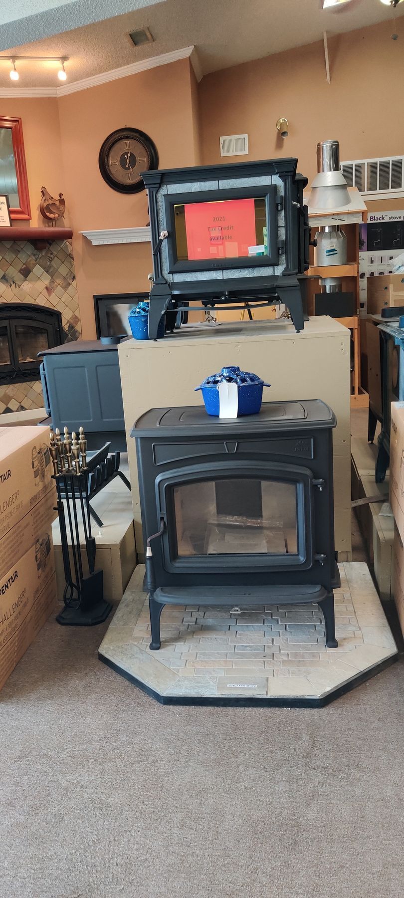 Wood stoves in a showroom, one on a riser, with fire tools in front.