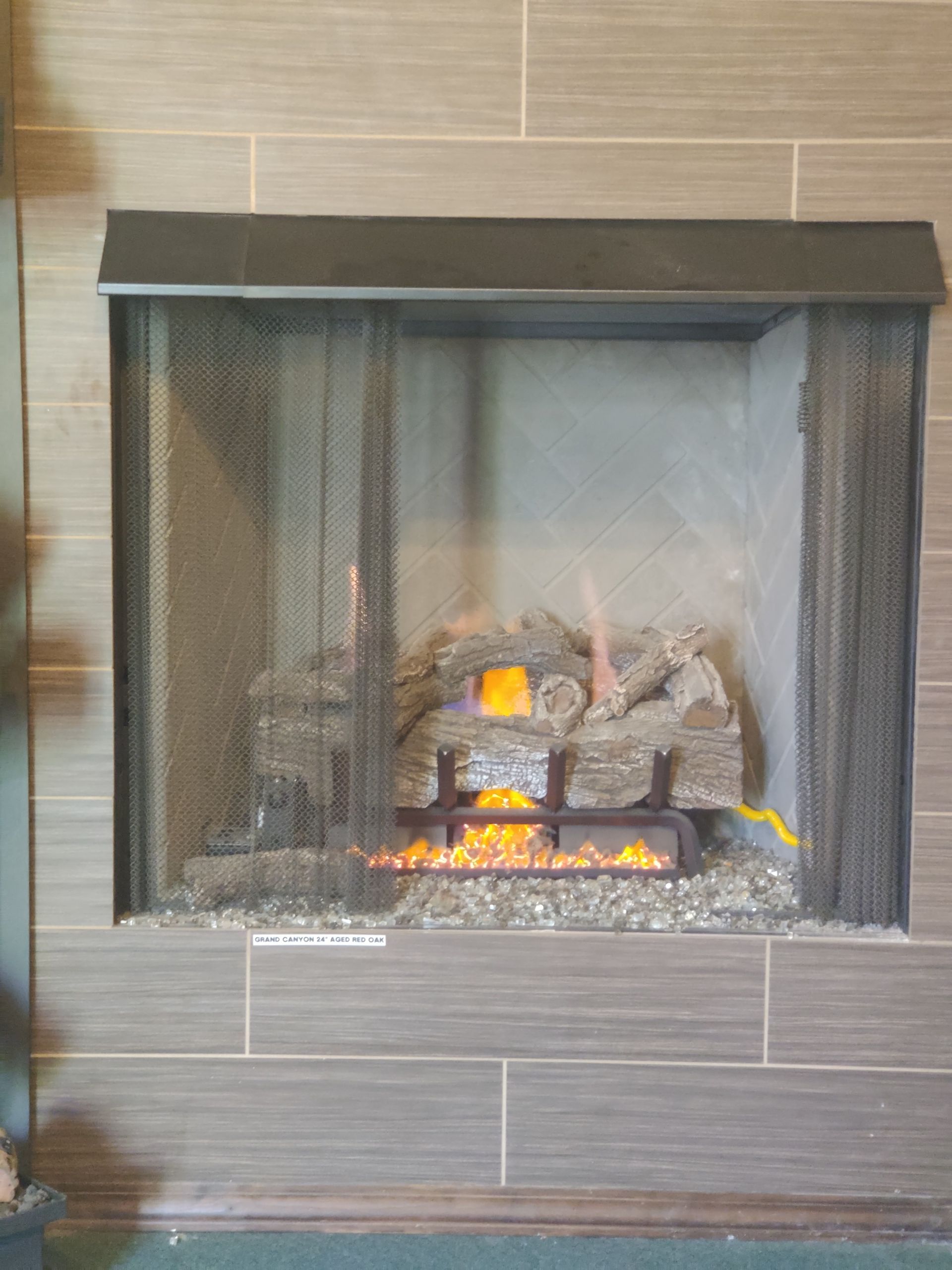 Gas fireplace with burning logs, inside a stone-tiled surround and metal screen.