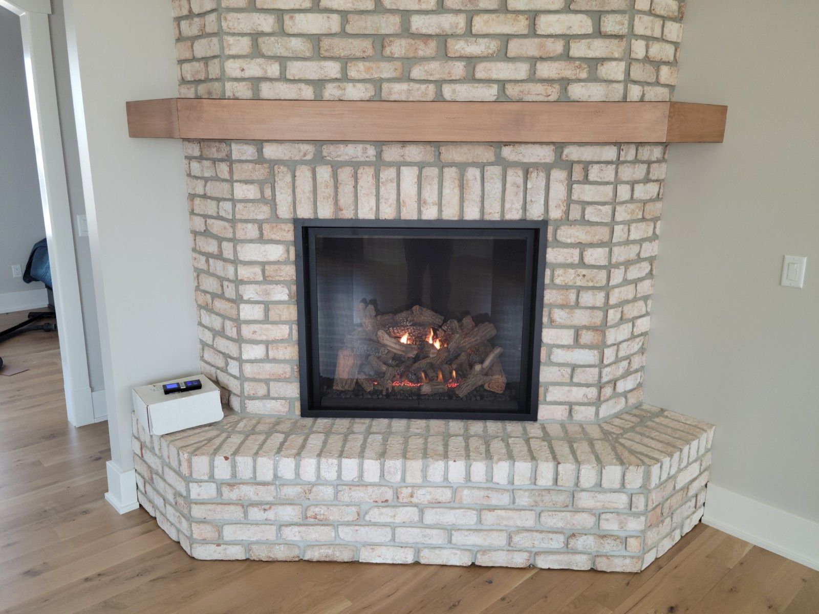 Fireplace with tan brick, black insert, wooden mantle, and hardwood floor.