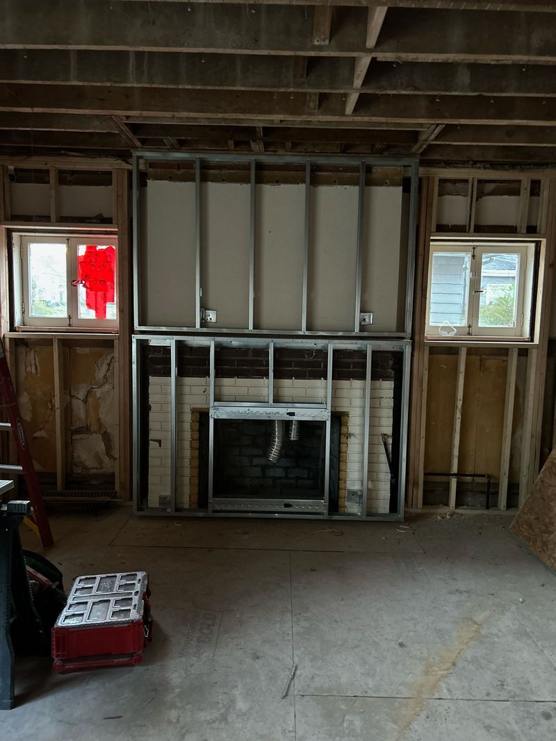 Basement with fireplace under construction, metal framing, windows, and partially finished walls.