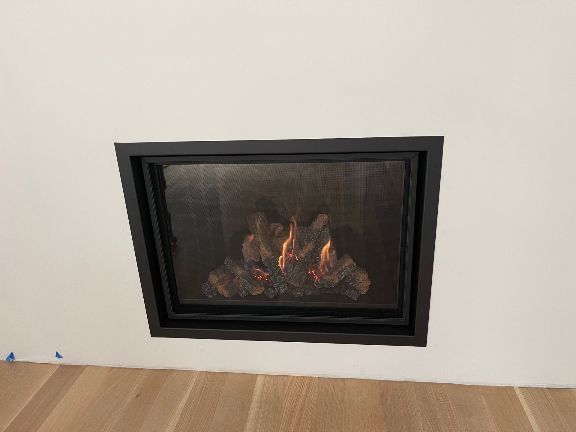 Black framed fireplace with flames in white wall setting.