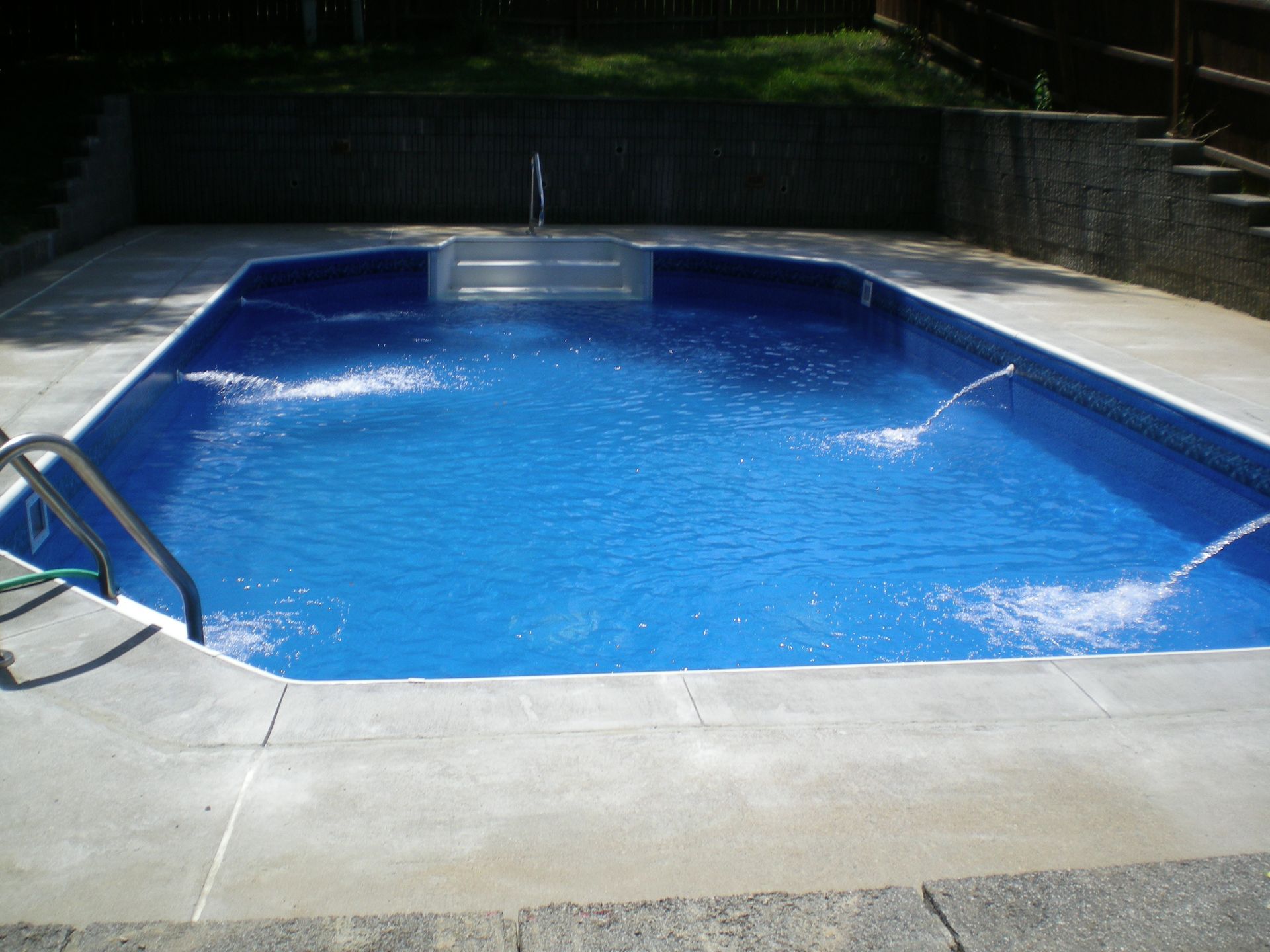 Blue swimming pool with water jets and concrete surround.