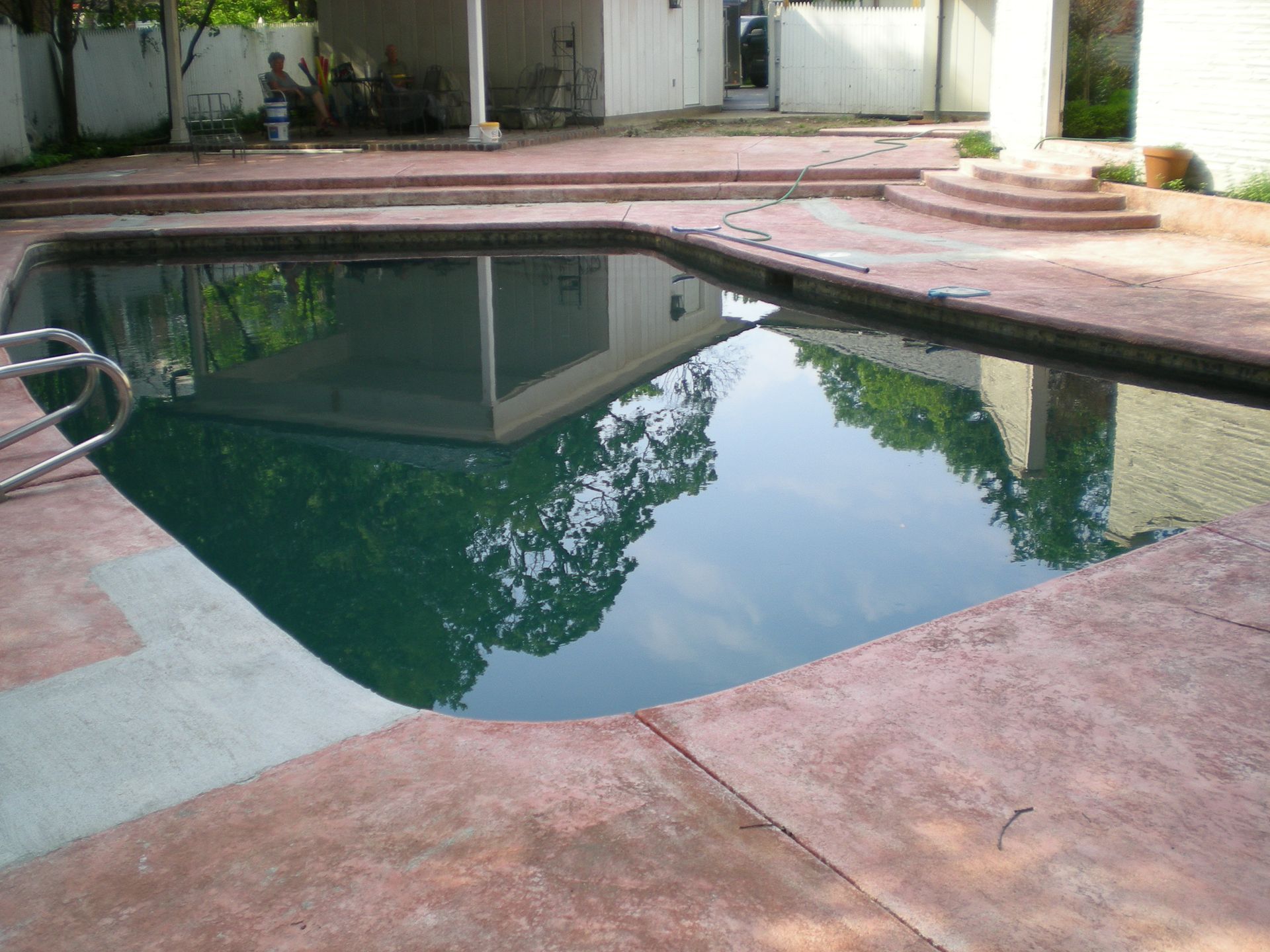 Swimming pool with dark water, red concrete deck, and building reflections.