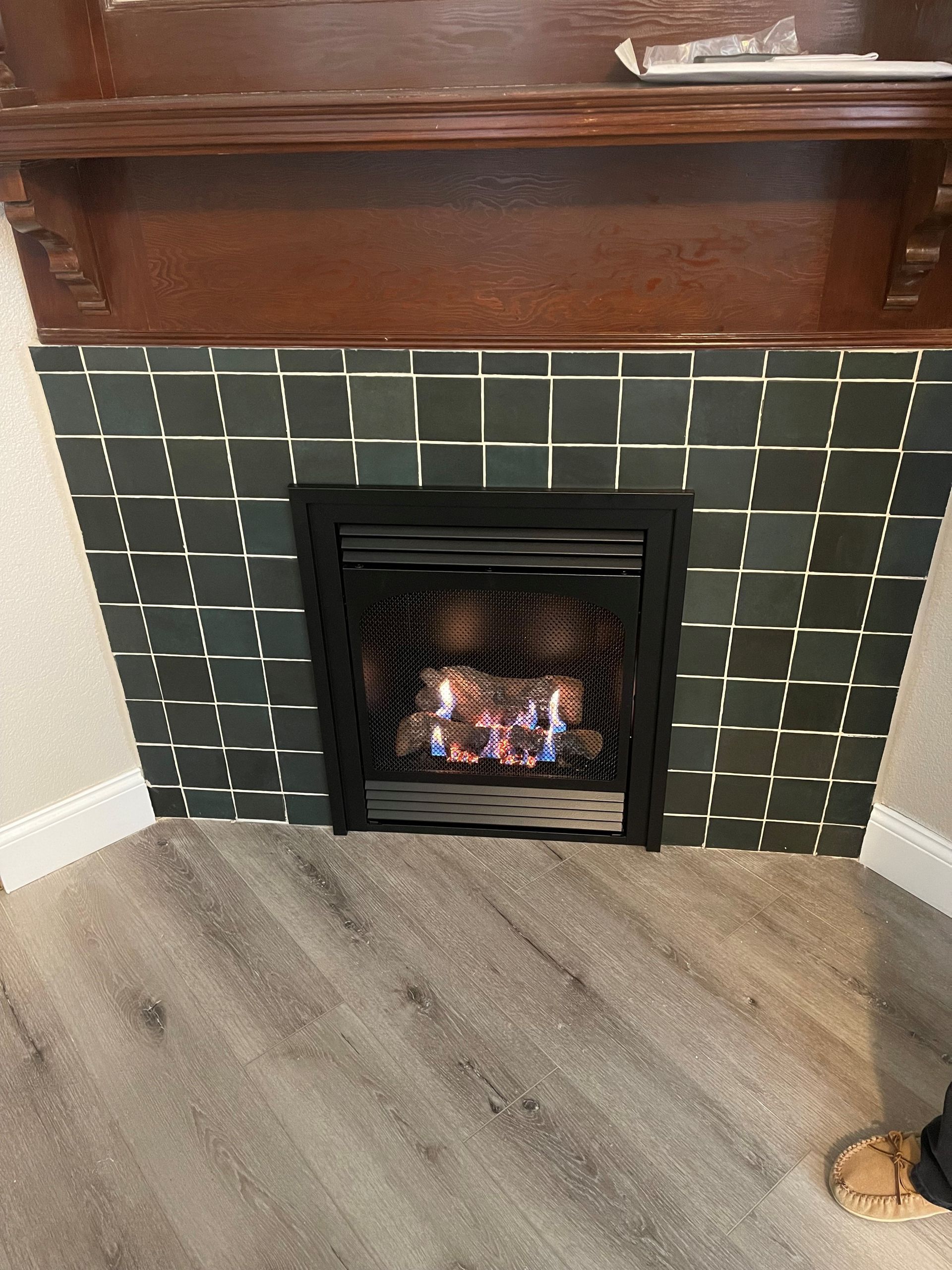 Fireplace with a black metal frame and a fire burning inside, surrounded by dark green tiled wall.