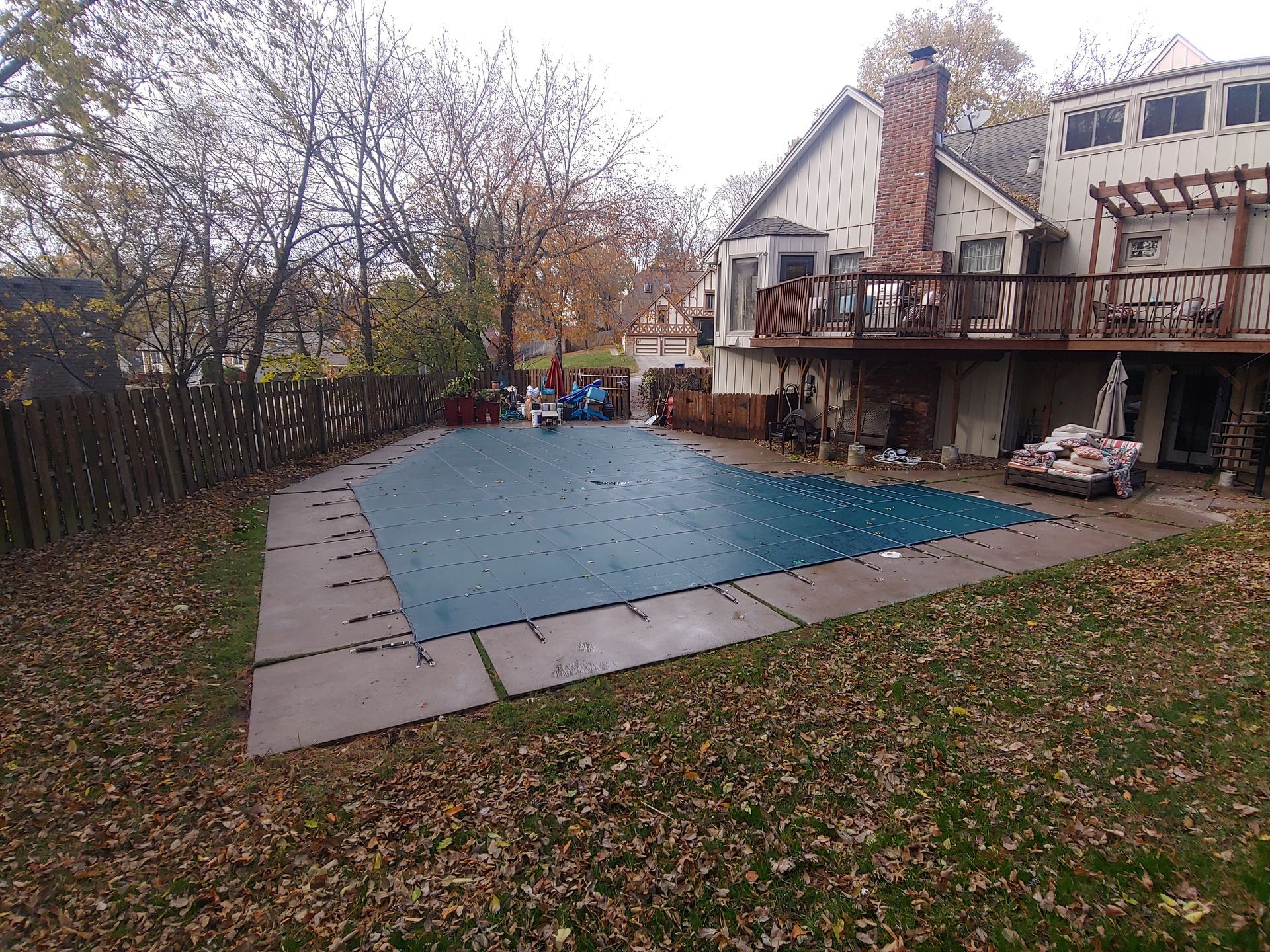 A backyard pool covered in blue tarp with a wooden deck and house in the background.