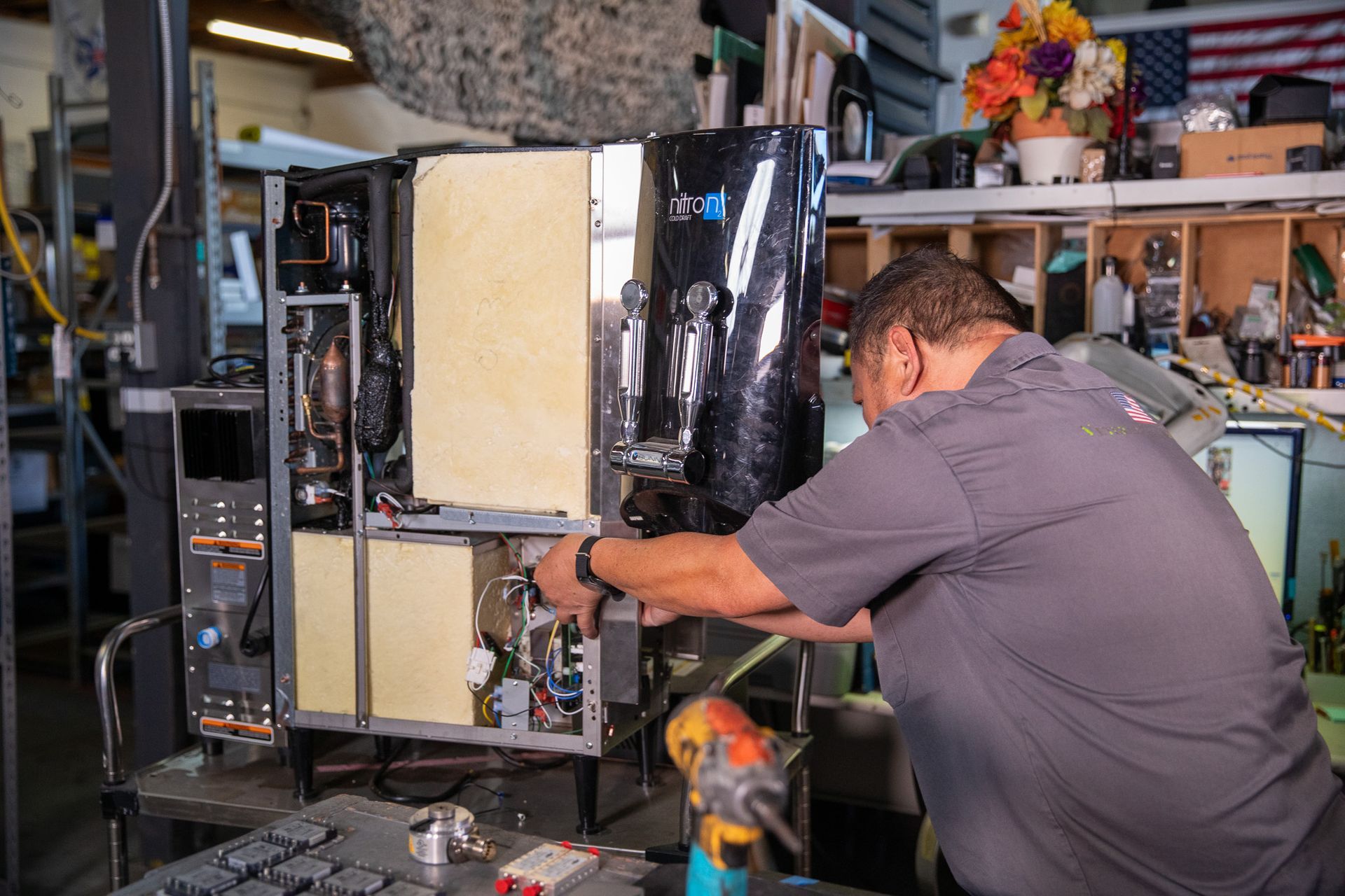 Man repairing a black machine with exposed interior components in a workshop.