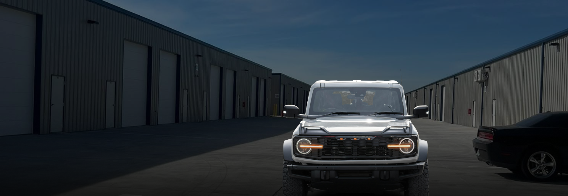 A silver SUV driving toward the viewer on a dark street, warehouses on both sides | Axe-A-Dent Auto Collision