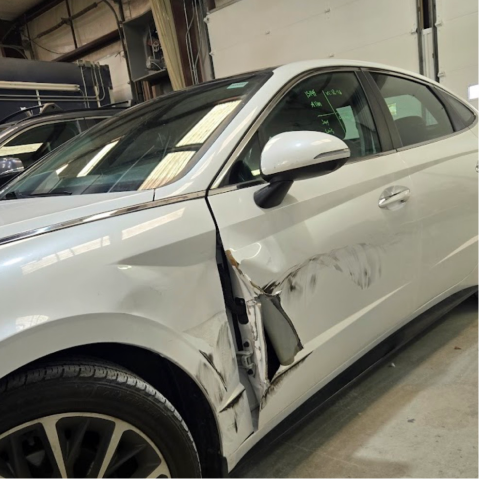 White car with significant damage to the driver's side door and panel in an automotive repair shop| Axe-A-Dent Auto Collision