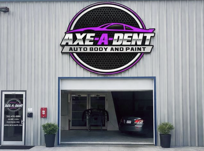 Exterior of Axe-A-Dent auto body shop with open garage door. Sign features a purple car silhouette and the name | Axe-A-Dent Auto Collision