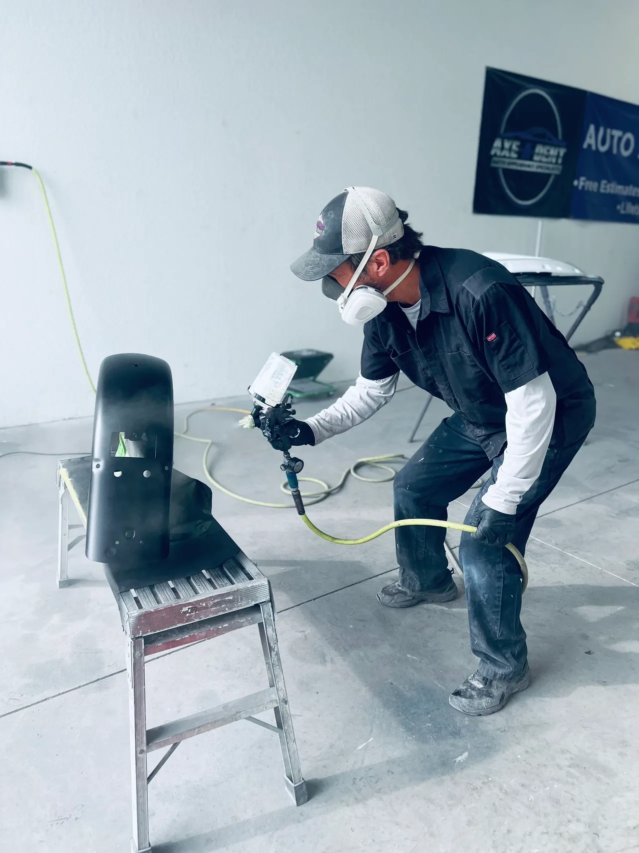 Person in overalls spraying a tire with a paint gun in a body shop | Axe-A-Dent Auto Collision
