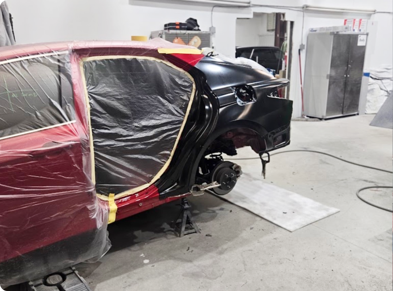 Car's rear partially repainted in black and red, body repair in a workshop. Plastic sheeting protects sections | Axe-A-Dent Auto Collision