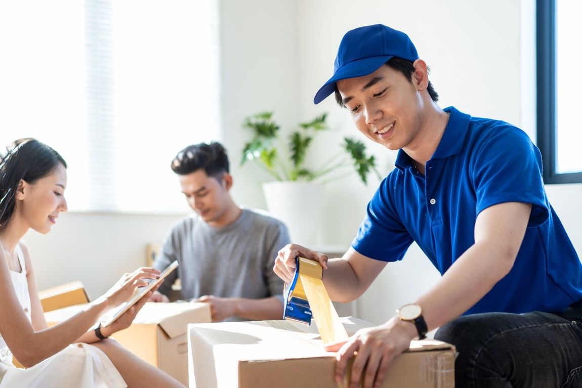 A man in a blue shirt is taping a box while a woman looks on.