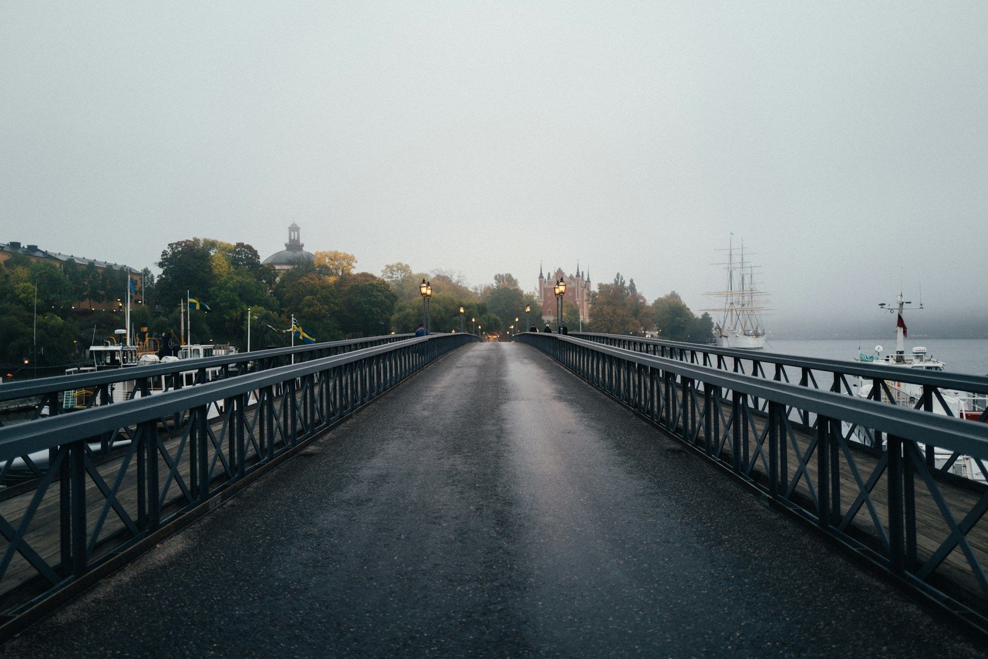 A wet asphalt bridge leads toward Skeppsholmen in Stockholm during autumn.