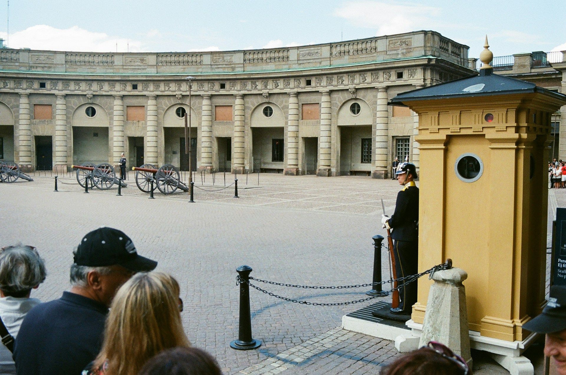 A guard in uniform stands by a sentry box in a cobblestone courtyard at the Royal Palace in Stockholm, Sweden.
