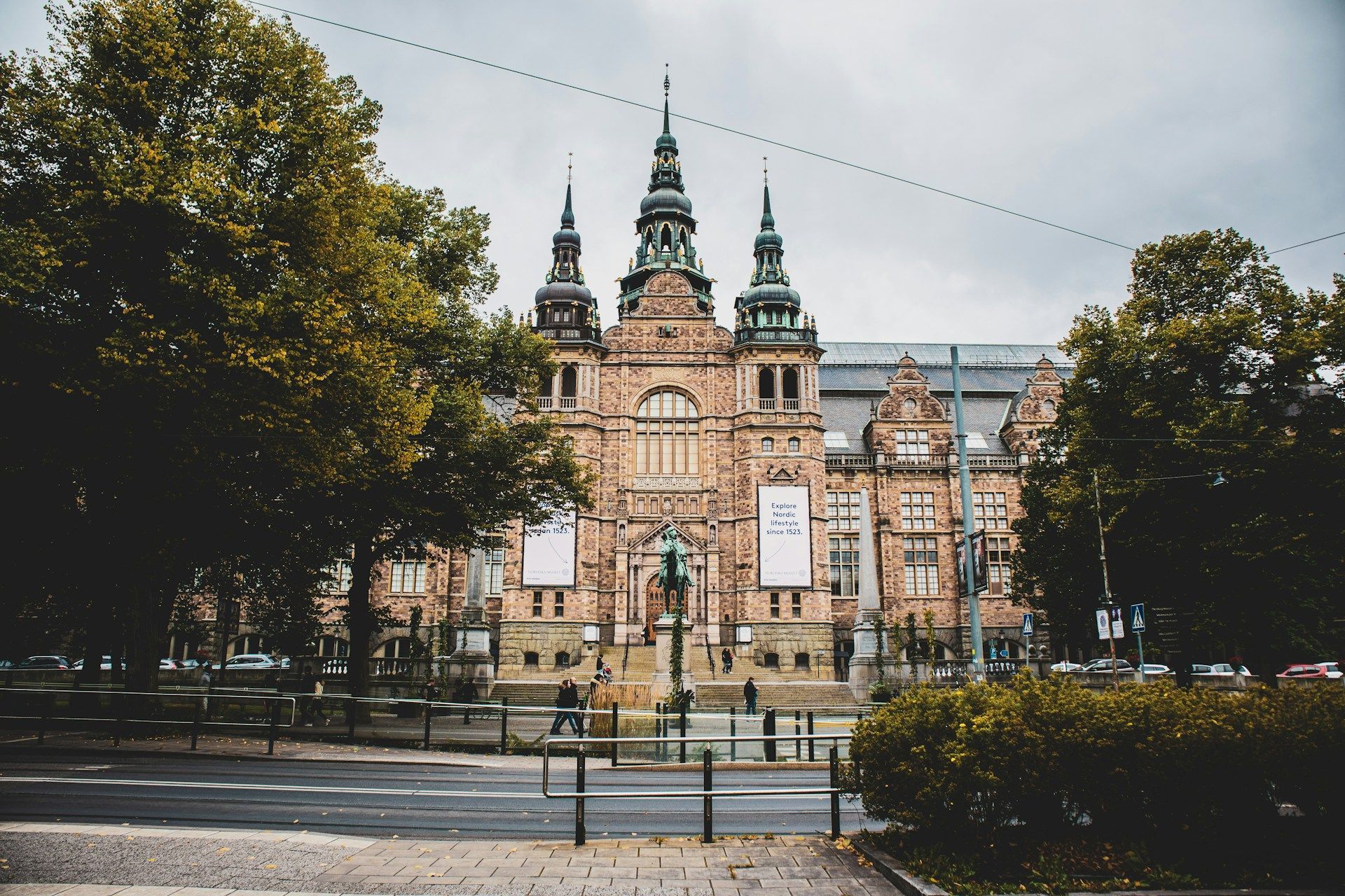 The Nordic Museum in Stockholm, Sweden, is a grand, stone Renaissance-style building surrounded by trees under a gray sky.