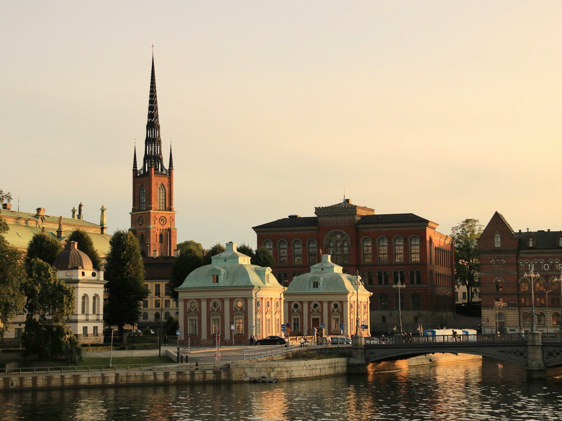 Riddarholmen Church spire rises over historic red-brick buildings and pale green-roofed houses.