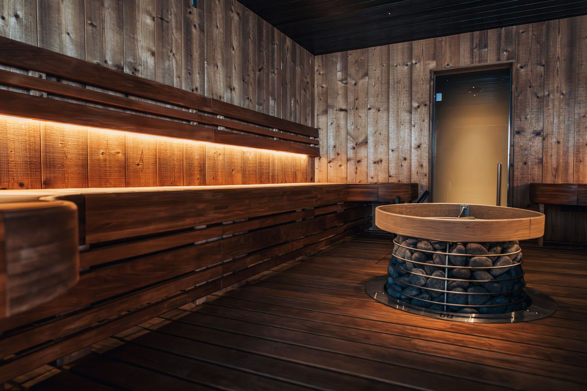 A sauna with the warm stones in the middle of the room and a long bench stretching to the far end